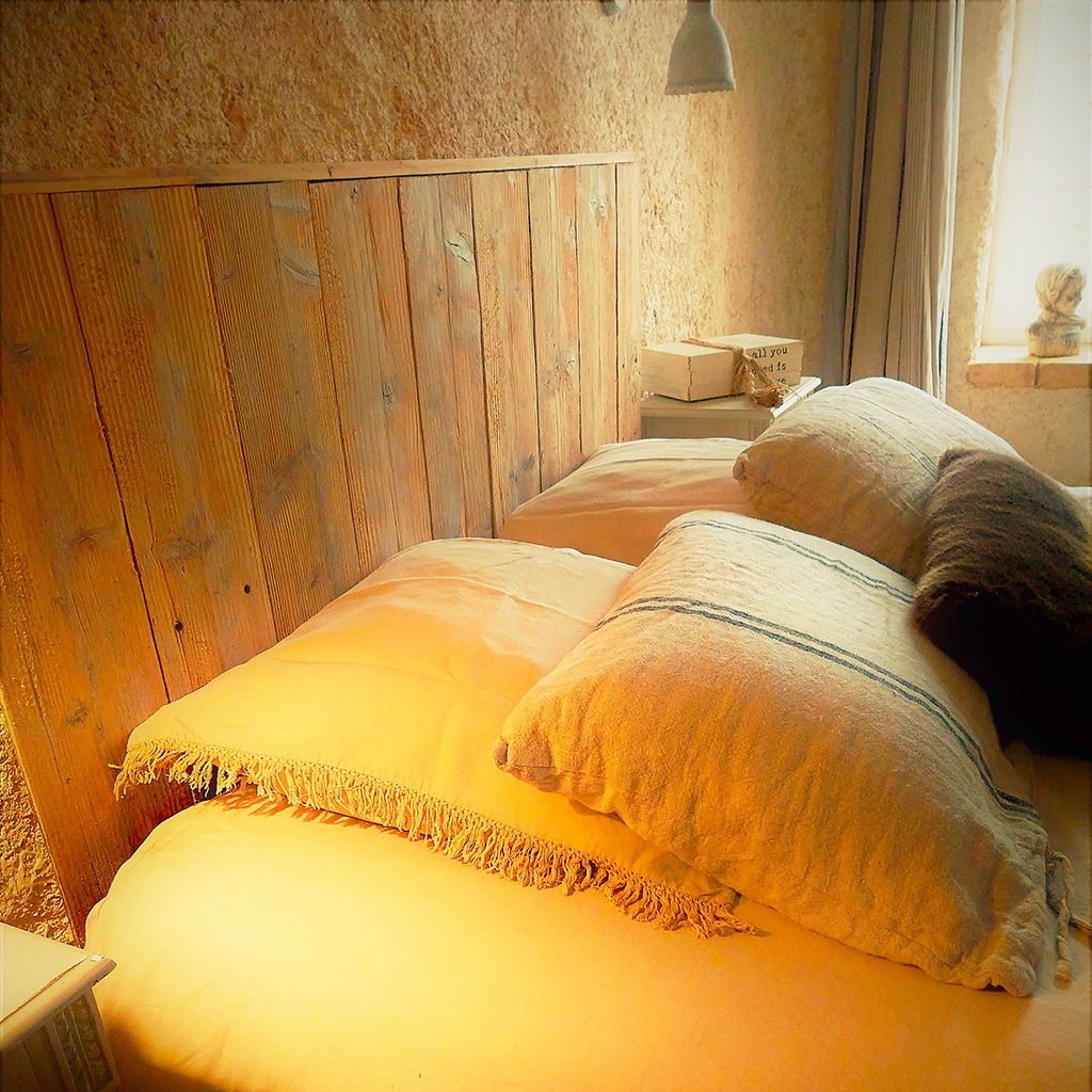 lit chambre lumière jaune avec oreillers lin mur pierre aparente Location gîte la Feuillade aux oiseaux à Laussou - Villeréal